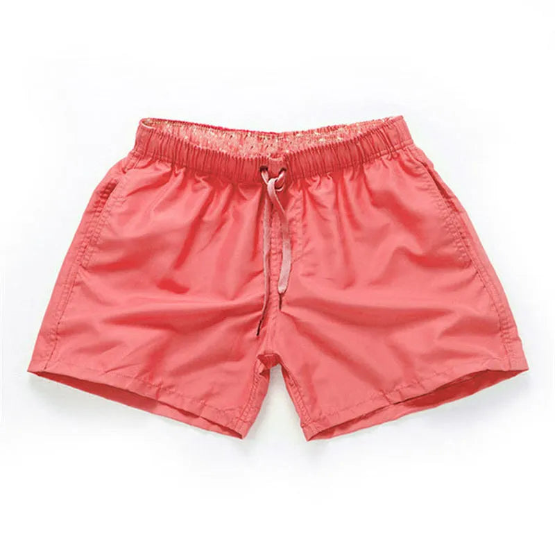 Men's straight-leg beach shorts in emerald green colour on a beach background.