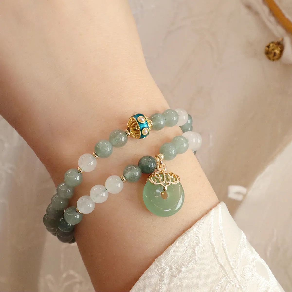 Close-up of a women's Myanmar jade bracelet with a traditional Chinese safety buckle pendant and geometric lucky bead charm.