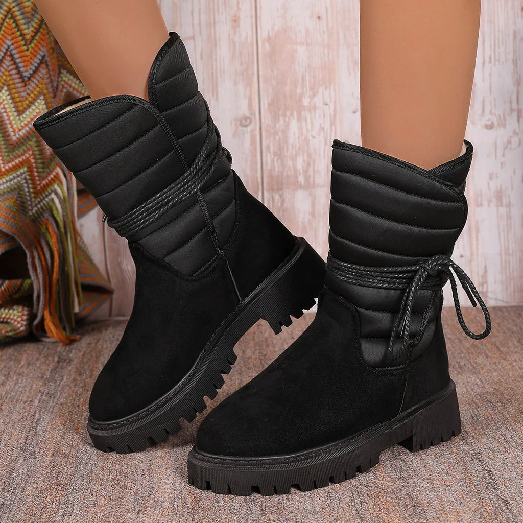 Women's black suede chunky heel snow boots with lace-up front and fleece lining shown on a winter background.