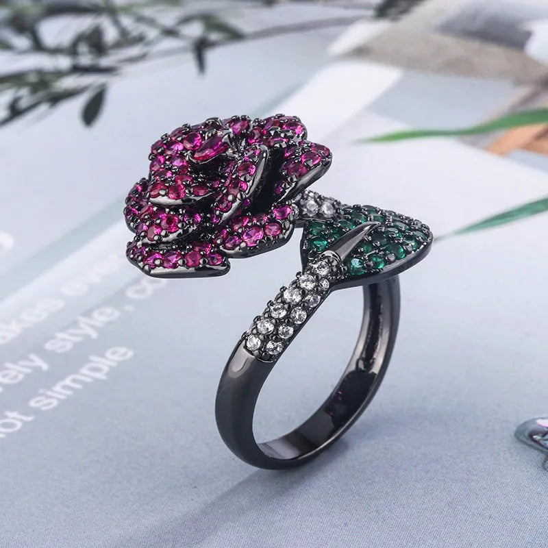 A black gold geometric flower ring with simulated red corundum stones on a model's hand.