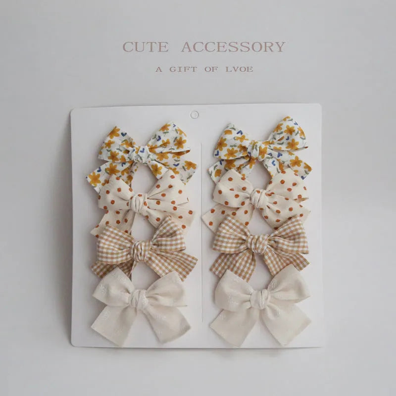 Children's fabric bow hairclip set showing eight different colour patterns including polka dots and floral designs