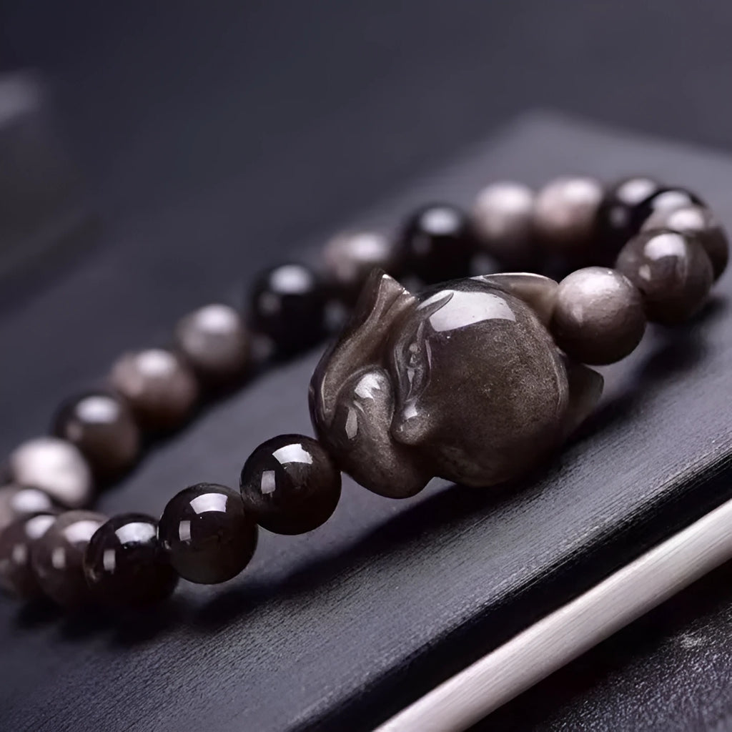 Close-up of a polished black obsidian bracelet bead carved with a detailed fox design.