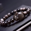 Close-up of a polished black obsidian bracelet bead carved with a detailed fox design.