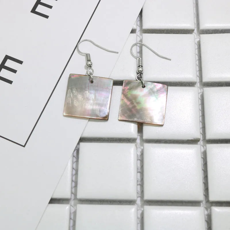 Handmade women's shell earrings in rectangular and square geometric shapes on a neutral background.