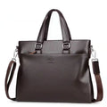 Men's black PU leather shoulder messenger bag with splicing design on a table.