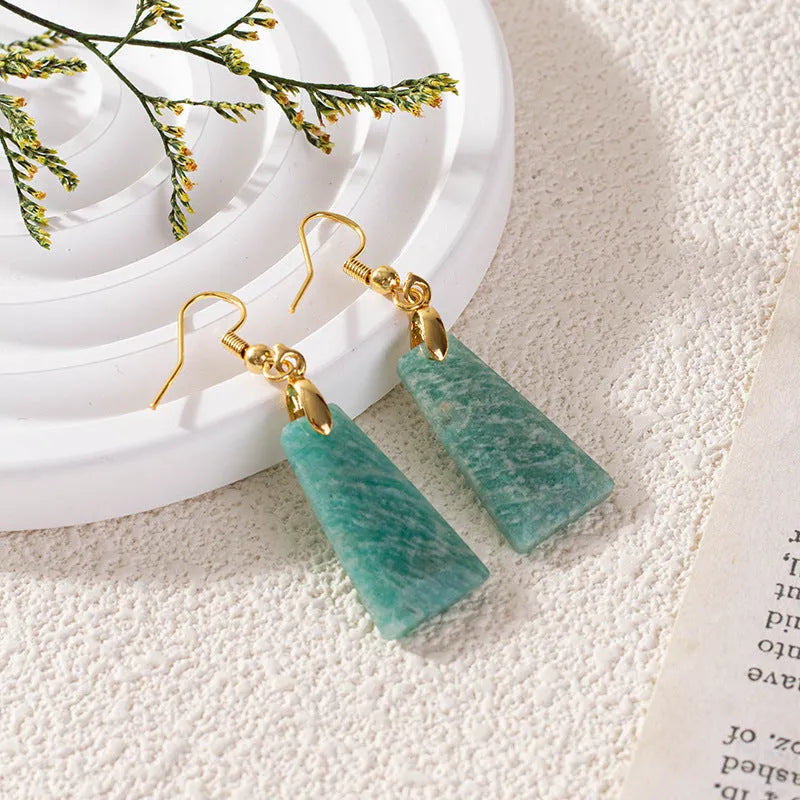 Gold trapezoid earrings with rough-cut amazonite stone and geometric detail on white background.