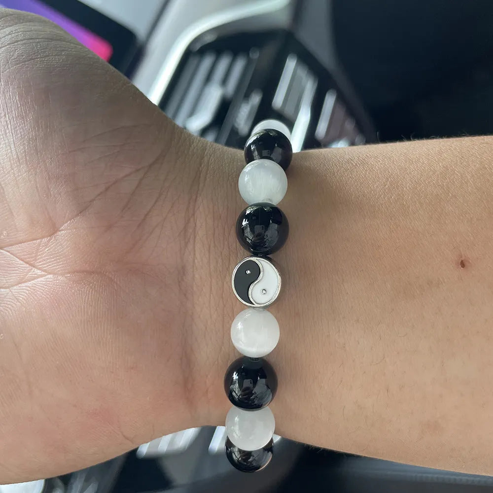 Close-up of a polished opal Tai Chi beaded bracelet with black agate ornamentation on a wrist.