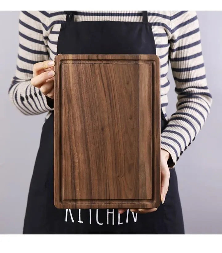 Solid black walnut wood cutting board with juice groove and side handle on a kitchen counter