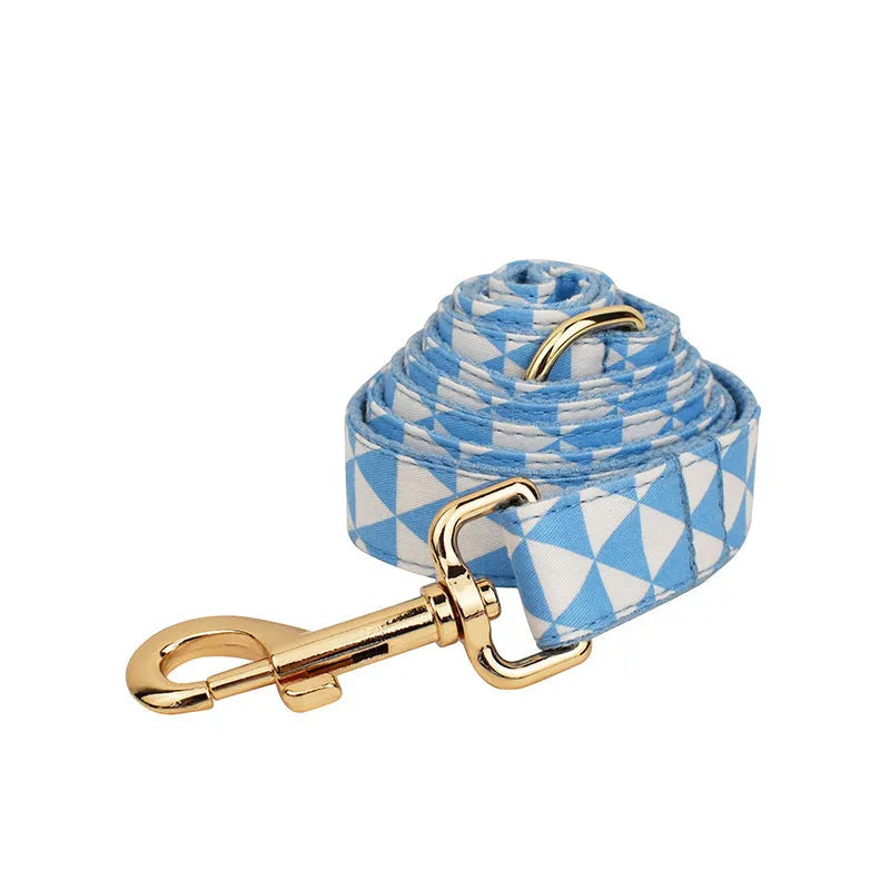 Blue cloth dog vest, matching collar with triangular ring, rope leash, and decorative bow laid out as a four-piece set.