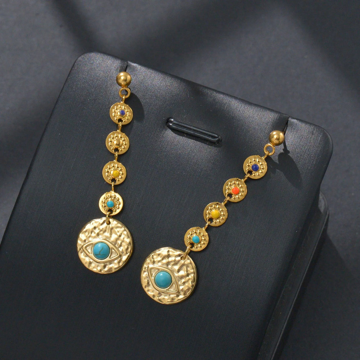 Three pairs of geometric stainless steel drop earrings showing Eight Awn Star, Eye, and Shell Sun designs