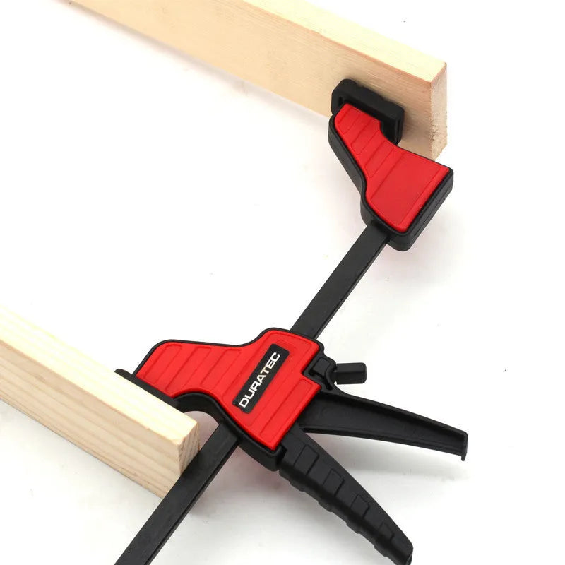 Black plastic quick release woodworking clamp with rubber jaws in multiple sizes on a workshop bench.