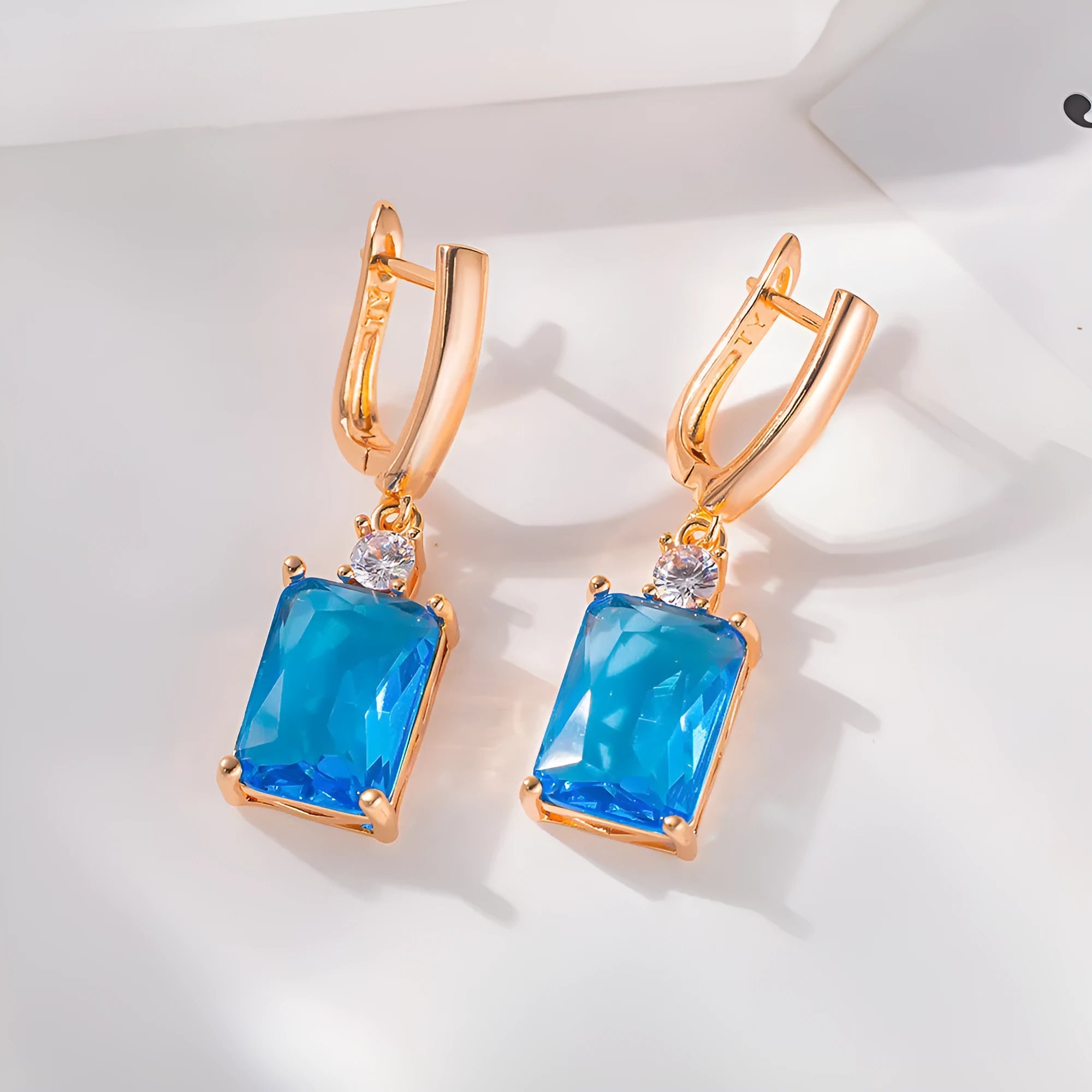 A pair of square-shaped gold-coloured earrings with a geometric design on a white background.