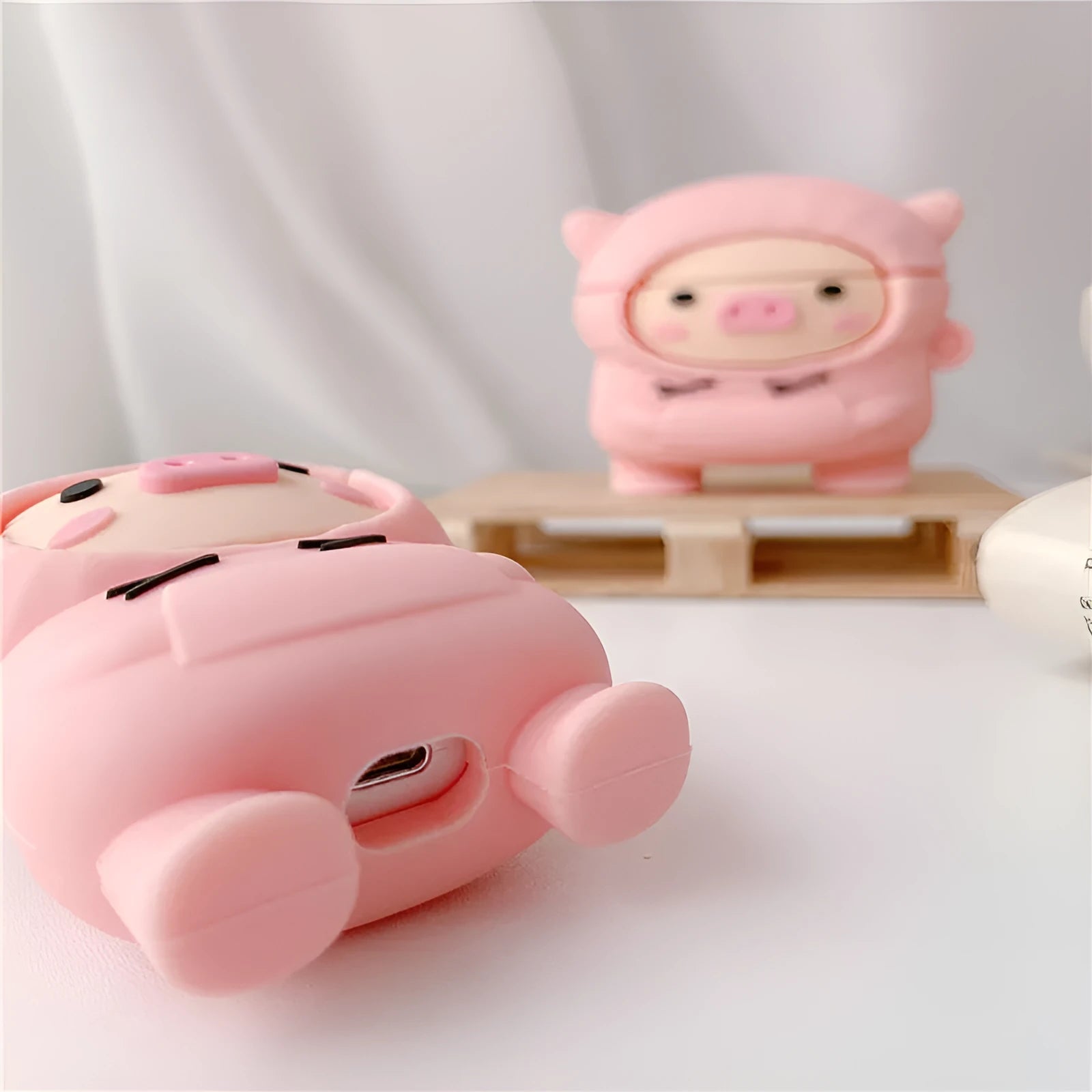 Pink silicone flip case with a cartoon pig design for AirPods and AirPods Pro, shown with a keychain hook.
