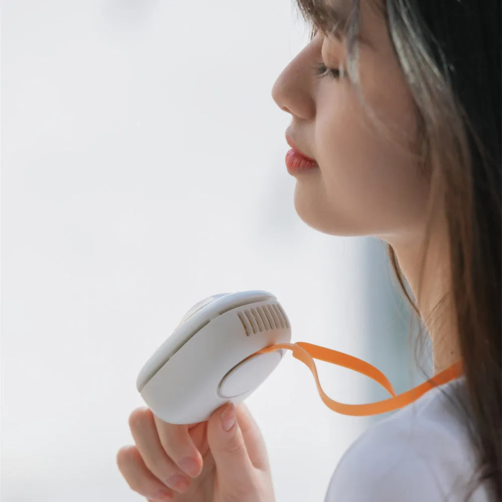 White handheld hanging neck fan with USB port and three speed buttons on a table.