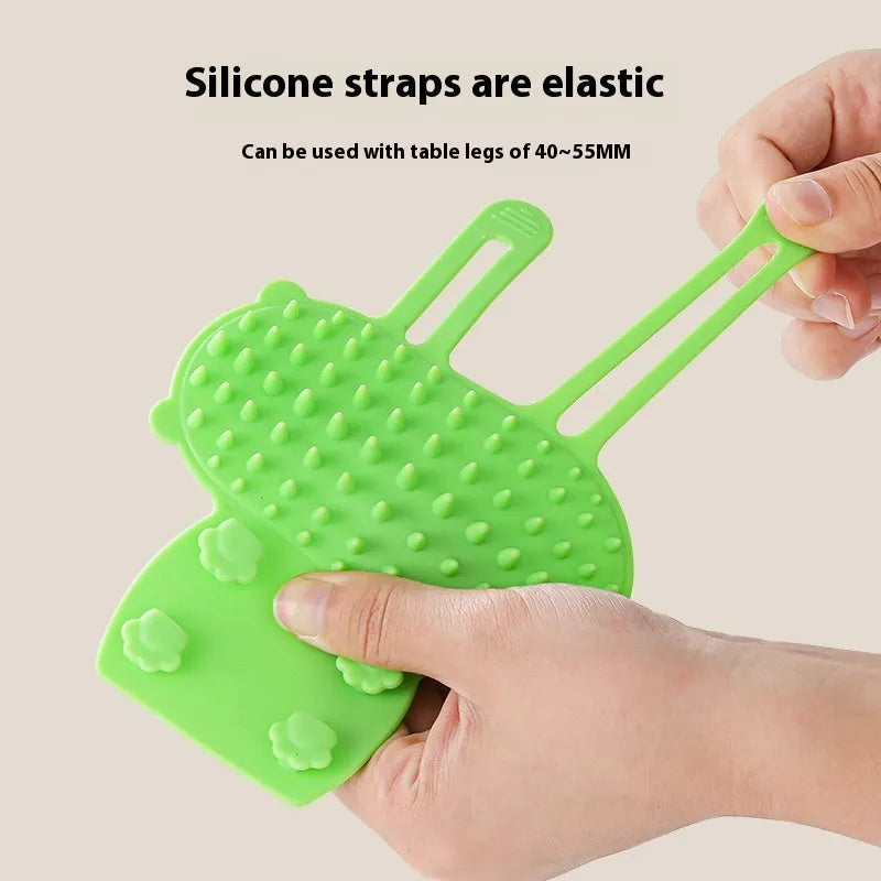 Silicone cat grooming comb with adjustable strap mounted on a table leg, shown in yellow.