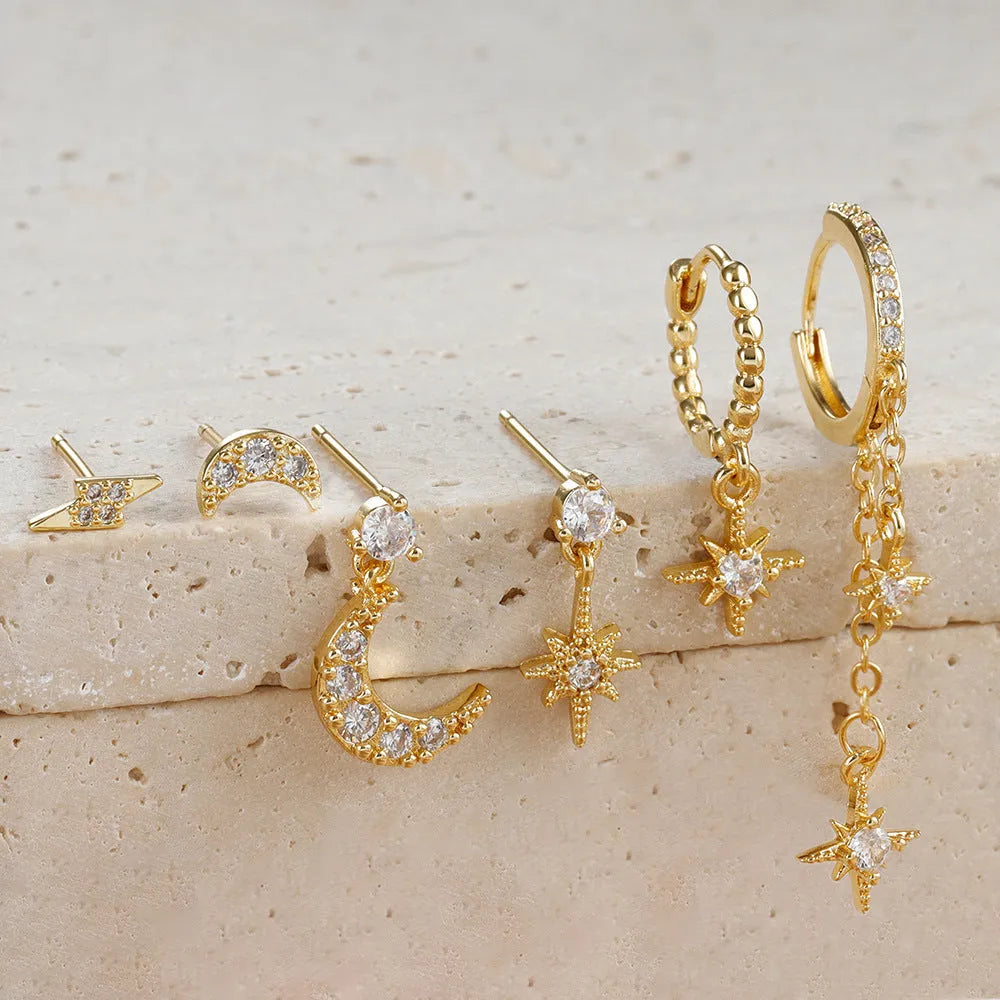 Set of six gold electroplated earrings with zircon studs and chain tassels on a flat surface.