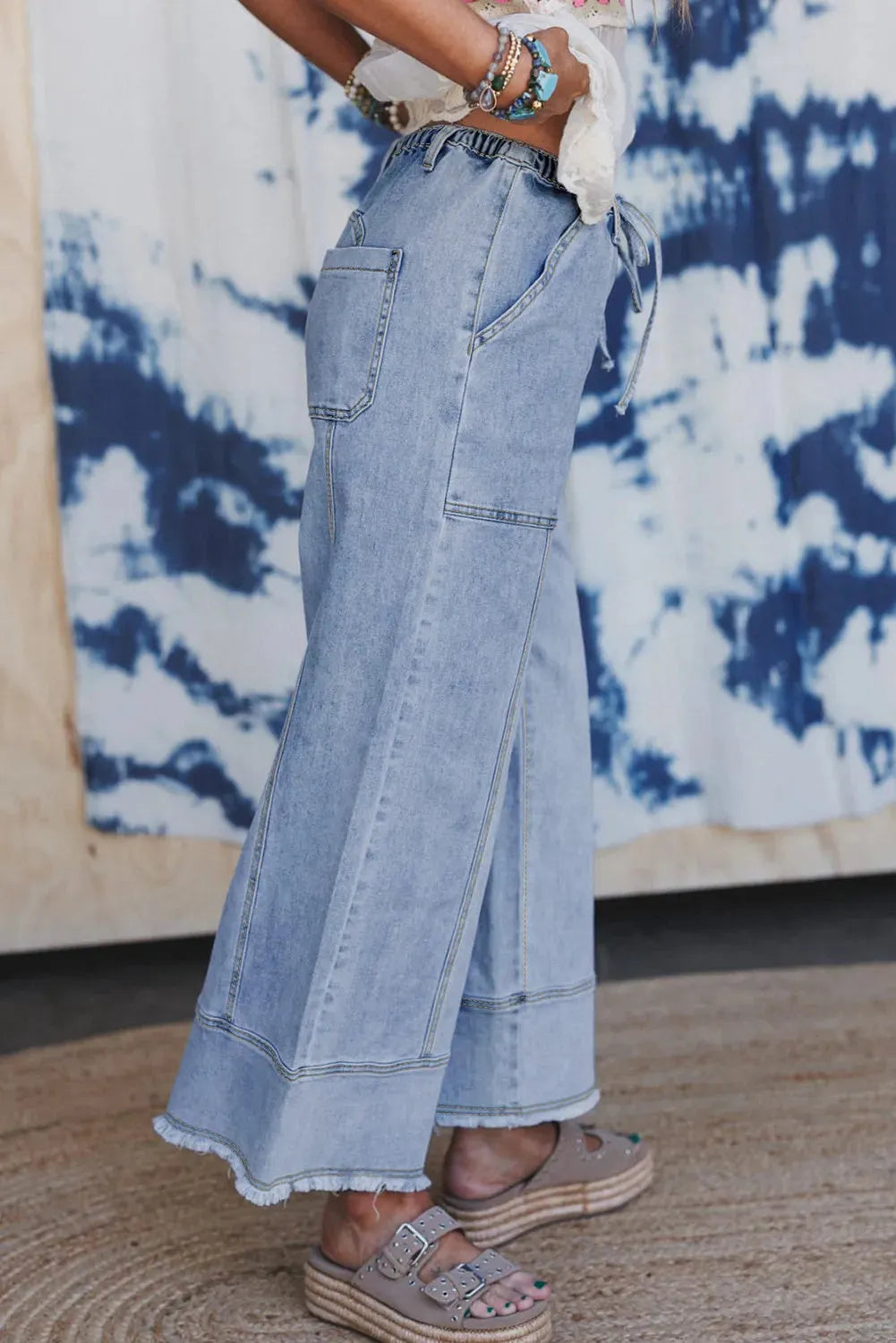 Beau blue women's wide-leg denim trousers with a drawstring waist and raw hem detail laid flat.