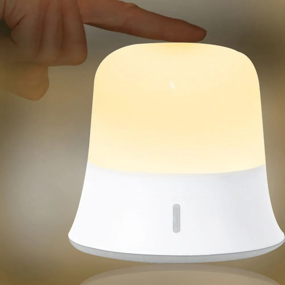 White baby night lamp with touch controls for dimming and colour change on a bedside table.