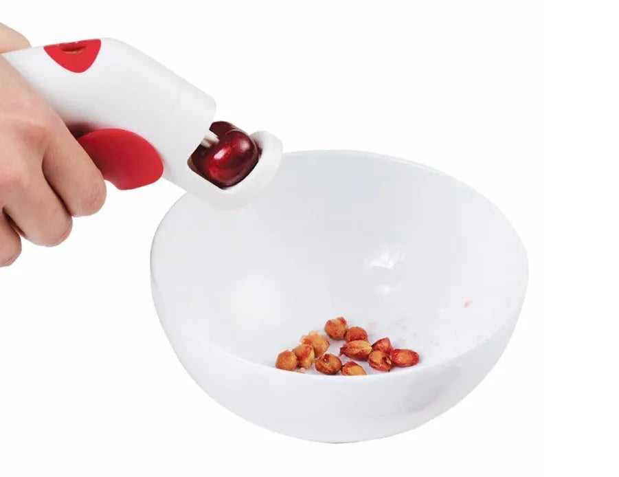 Stainless steel manual cherry pitting tool with ergonomic handle on a wooden surface.