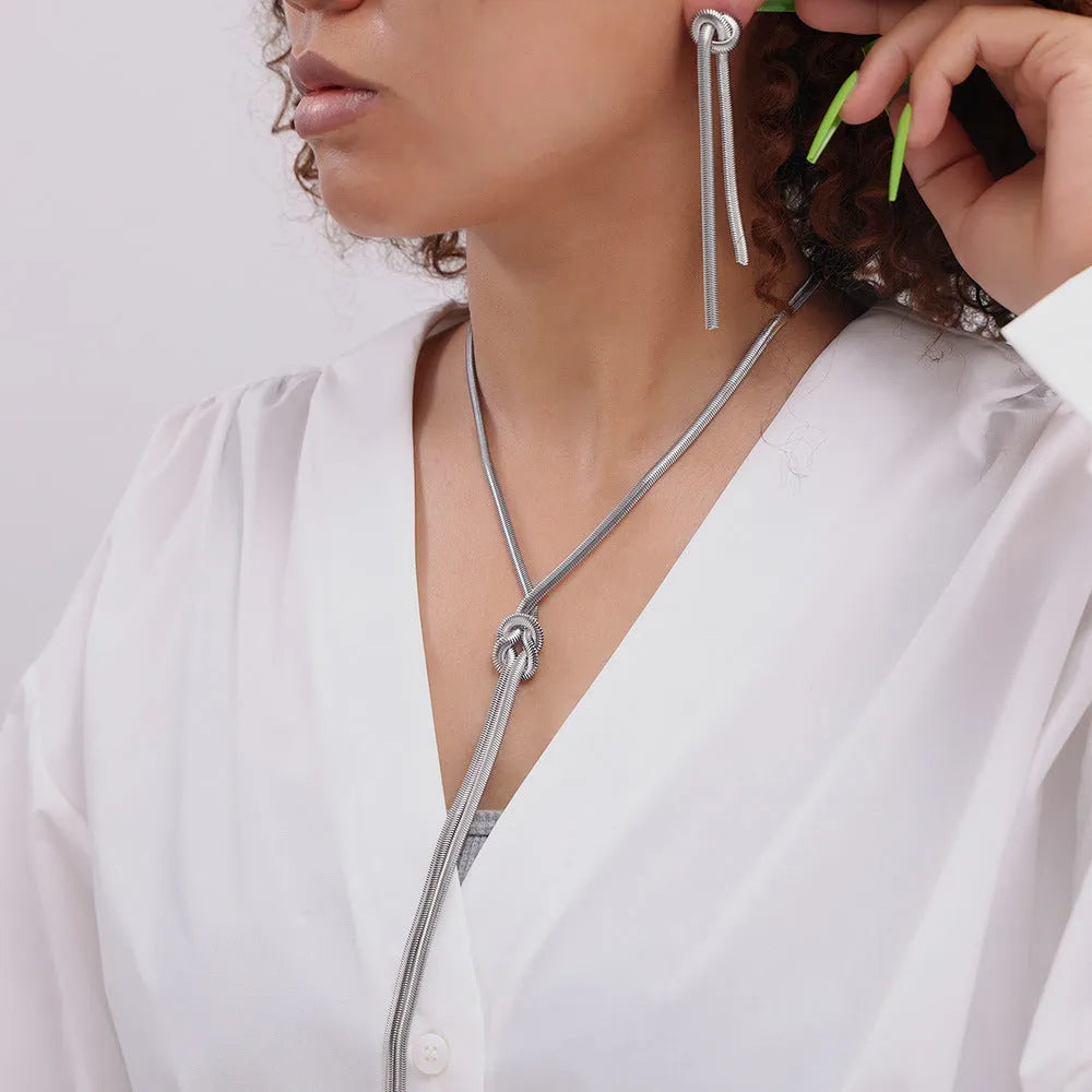 Gold colour titanium steel necklace with knotted tassel pendant and matching earrings on a white background.