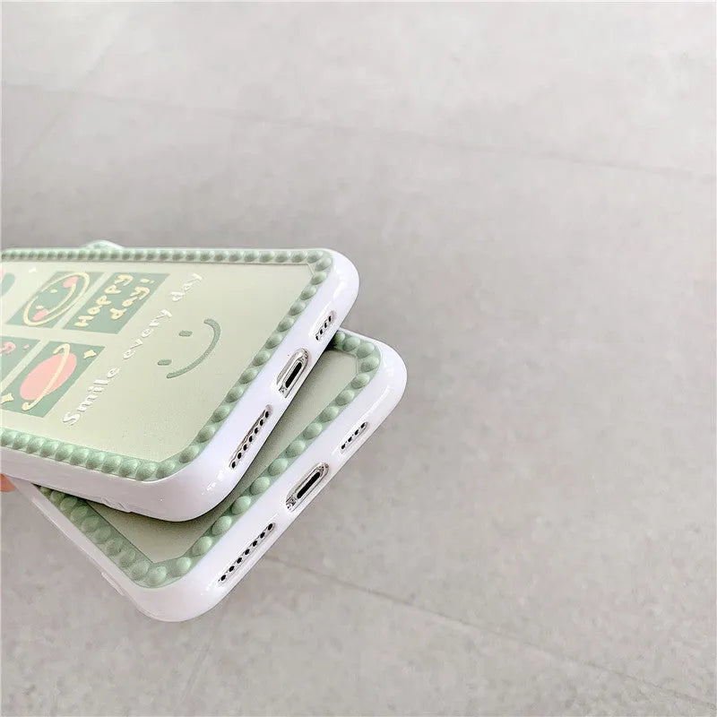 Green iPhone case with geometric smiley face pattern and polka dot border on a table.
