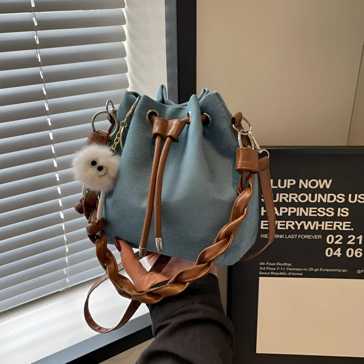 Blue synthetic leather cross body bucket bag with medium-soft structure and optional hanging ornaments