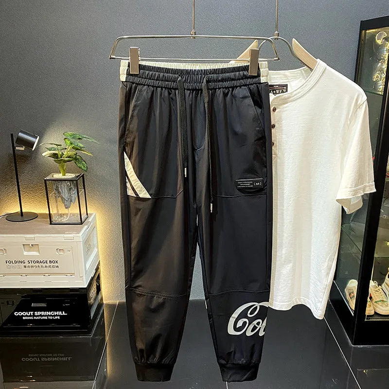 Black cotton men's cropped casual trousers with a banded ankle cuff laid flat.