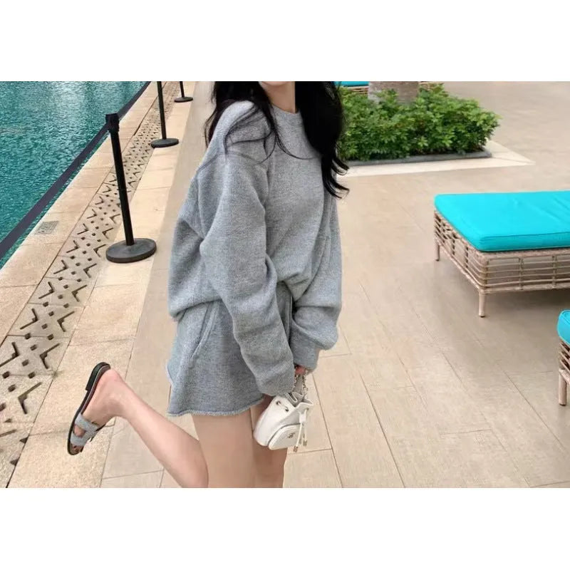 Woman wearing a loose grey long sleeve sweater and matching wide leg knit shorts lounge set.