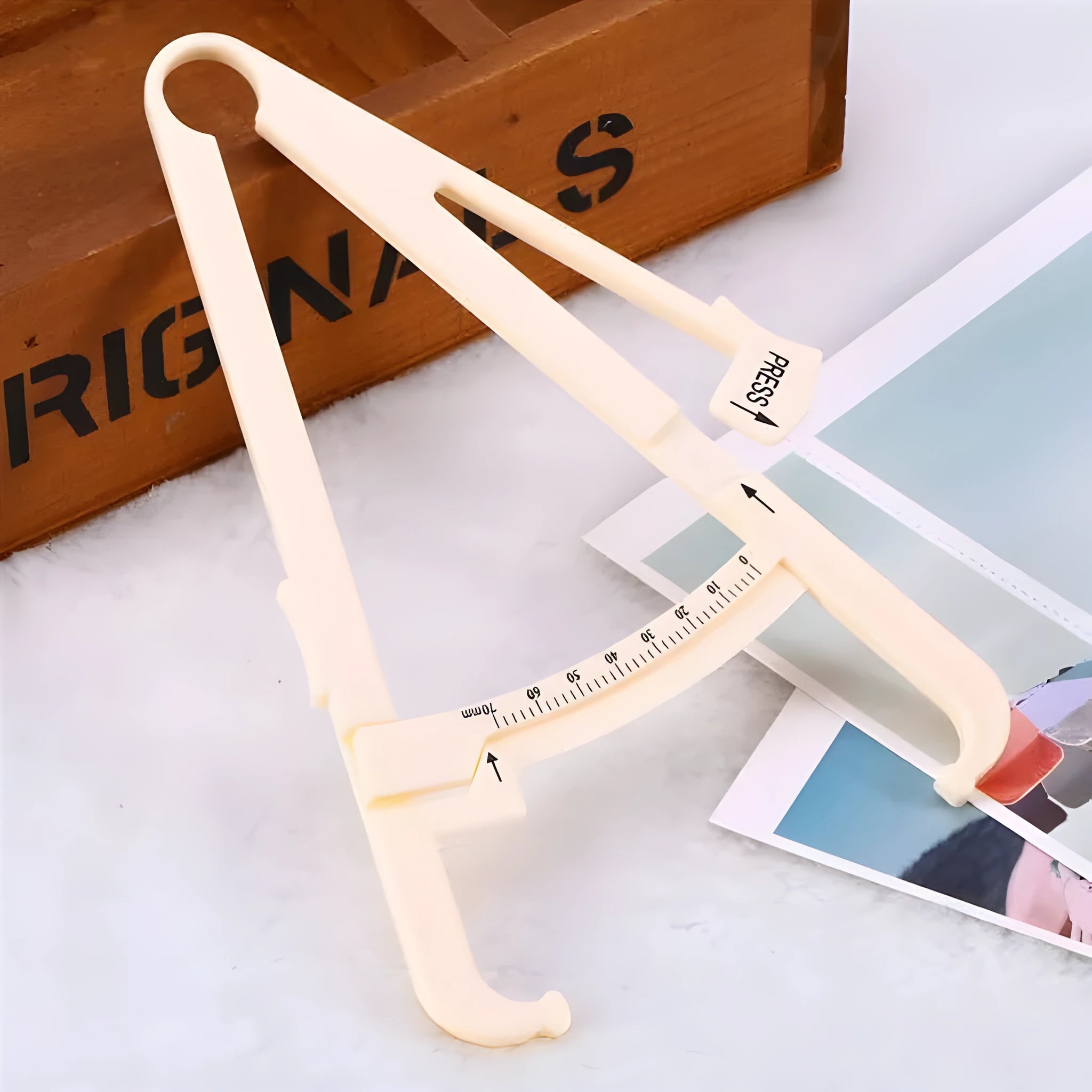 White acrylic body fat caliper skin fold thickness measuring tool on grey background.