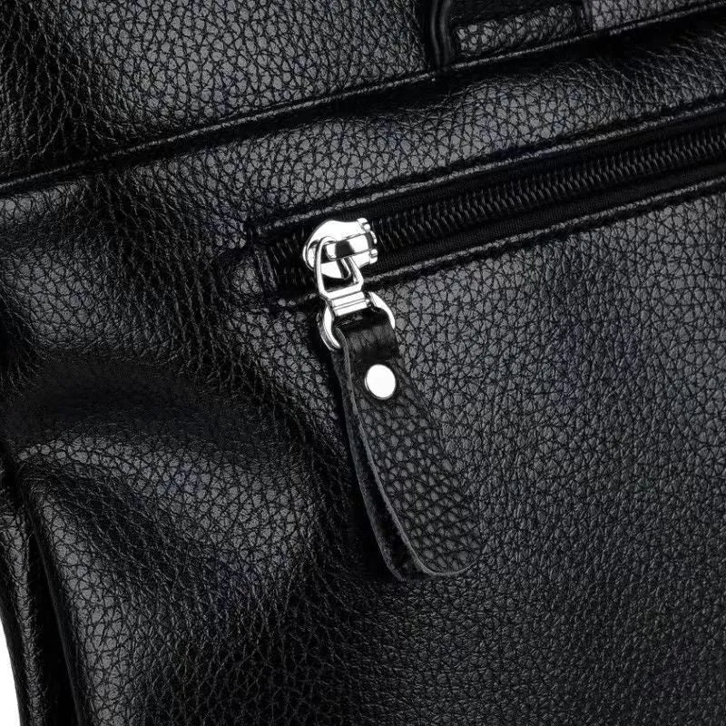 Men's black PU leather shoulder messenger bag with splicing design on a table.