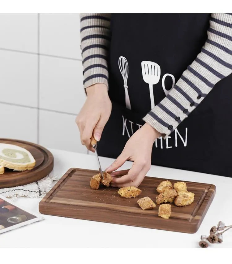 Solid black walnut wood cutting board with juice groove and side handle on a kitchen counter