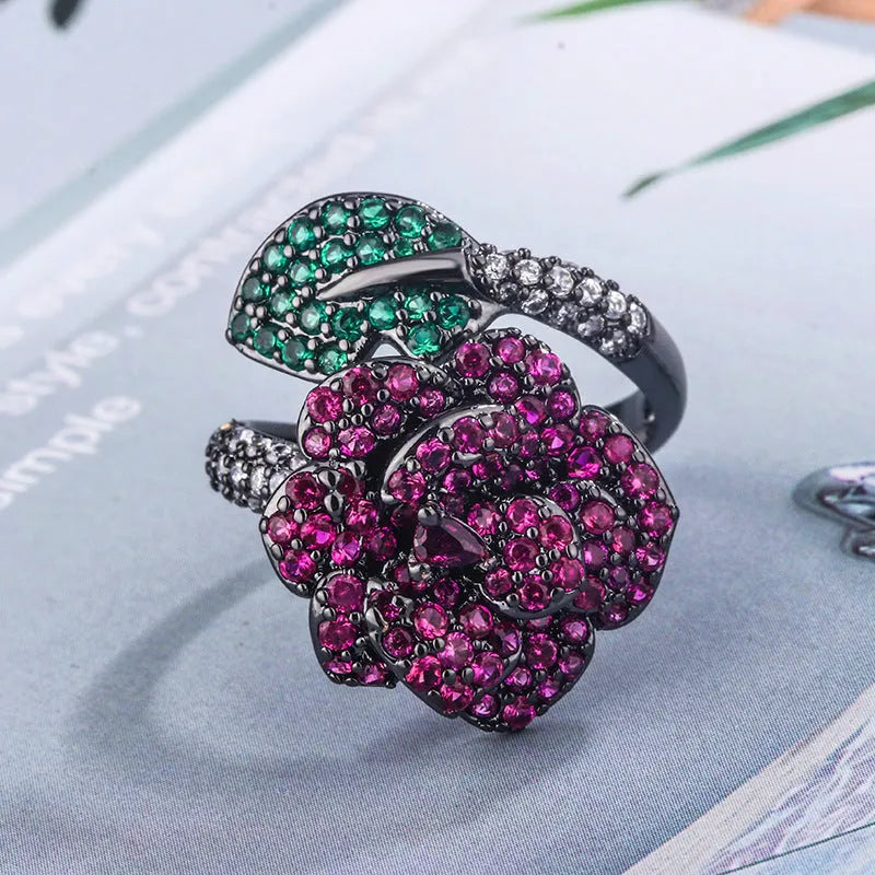 A black gold geometric flower ring with simulated red corundum stones on a model's hand.