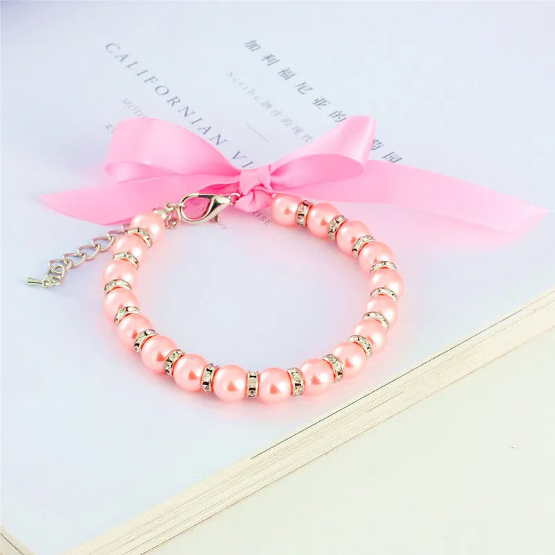 Small dog wearing adjustable pearl and rhinestone necklace with ribbon bow in pink colour