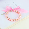 Small dog wearing adjustable pearl and rhinestone necklace with ribbon bow in pink colour