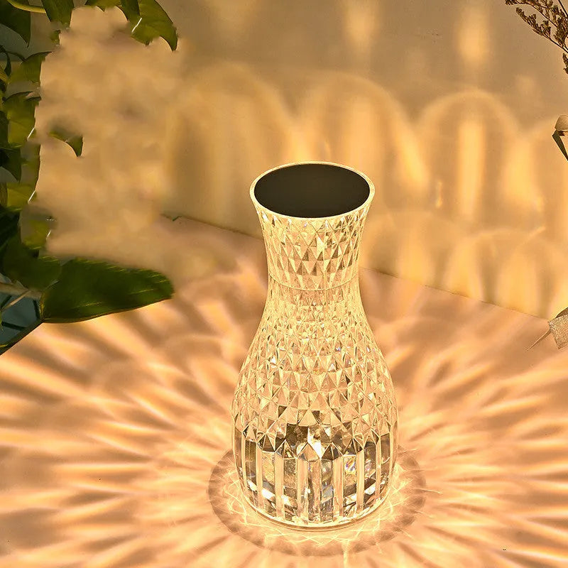 Transparent crystal vase shaped LED table lamp with remote control on a wooden bedside table.