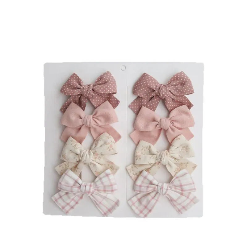 Children's fabric bow hairclip set showing eight different colour patterns including polka dots and floral designs