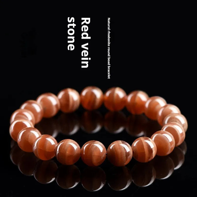 Natural old mine rhodochrosite round bead bracelet with ruyi design on a wrist.