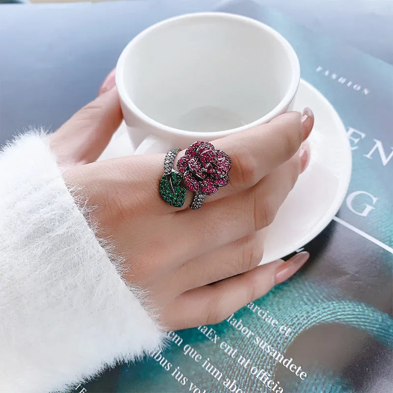 A black gold geometric flower ring with simulated red corundum stones on a model's hand.