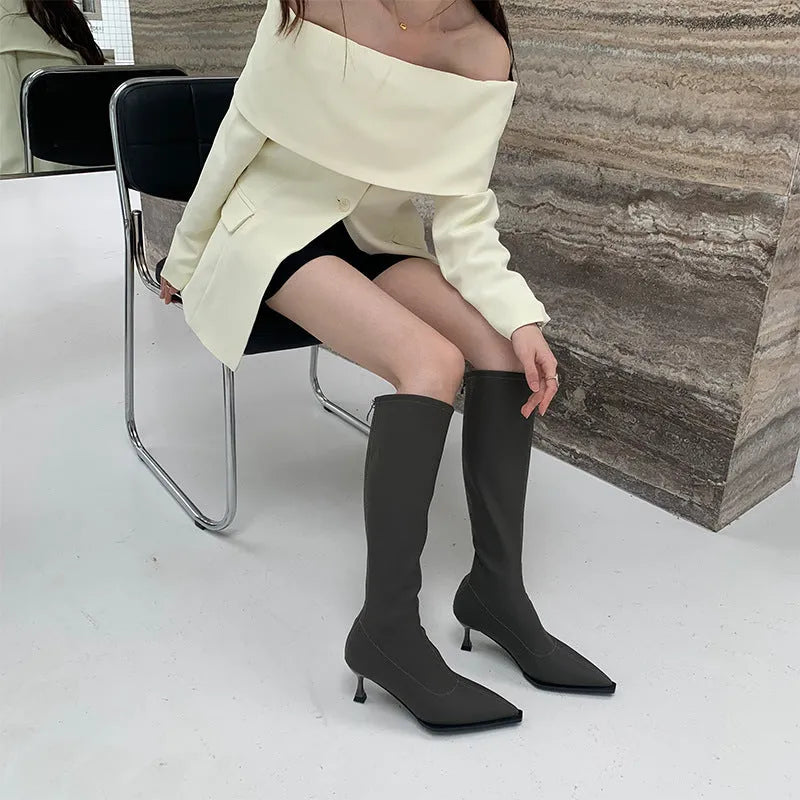 Women's black pointed toe below knee boots with back zipper and stiletto heel on grey background