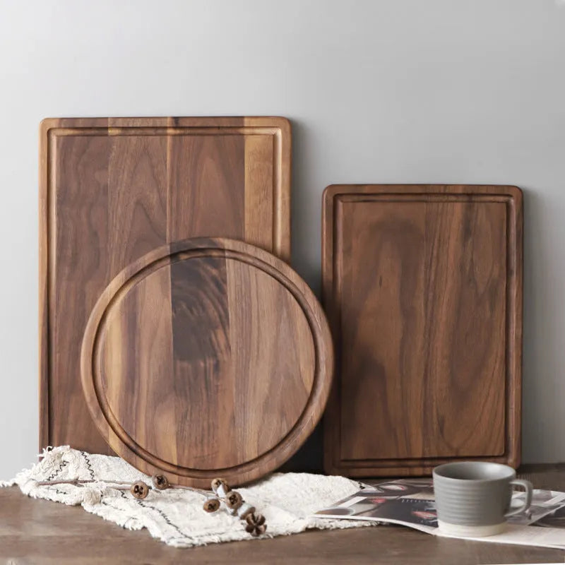 Solid black walnut wood cutting board with juice groove and side handle on a kitchen counter