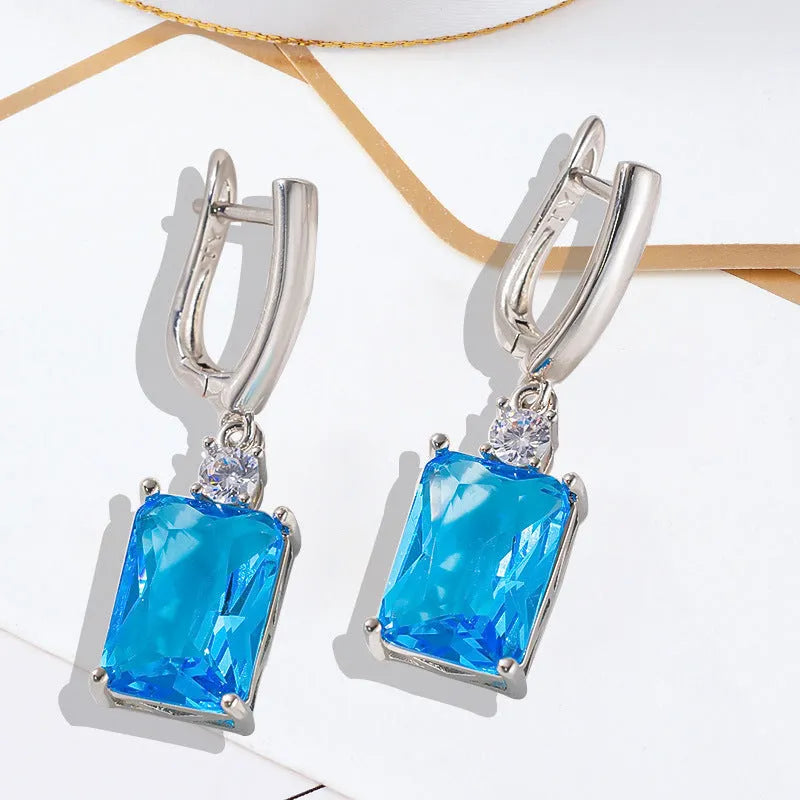 A pair of square-shaped gold-coloured earrings with a geometric design on a white background.