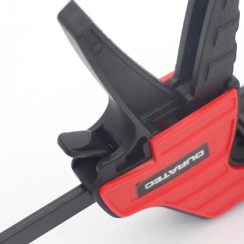 Black plastic quick release woodworking clamp with rubber jaws in multiple sizes on a workshop bench.
