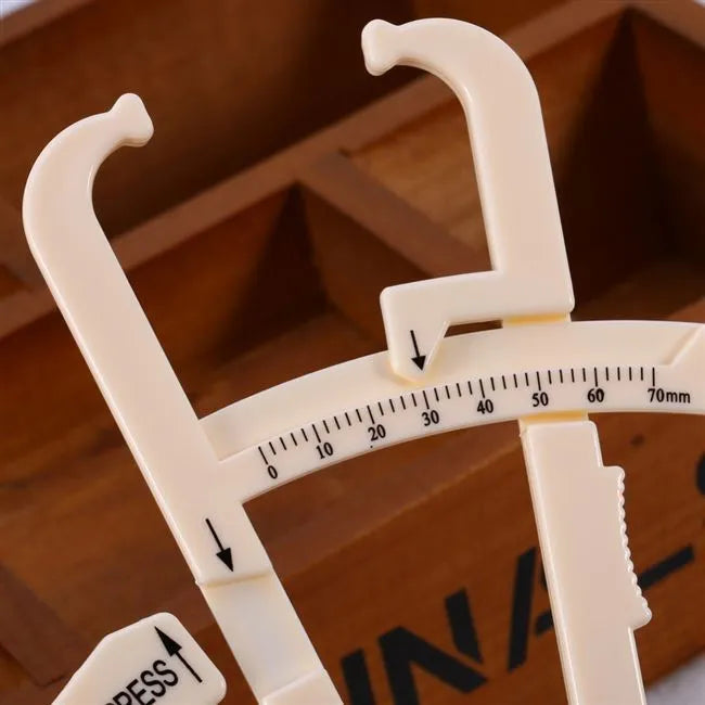 White acrylic body fat caliper skin fold thickness measuring tool on grey background.