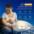 White baby night lamp with touch controls for dimming and colour change on a bedside table.