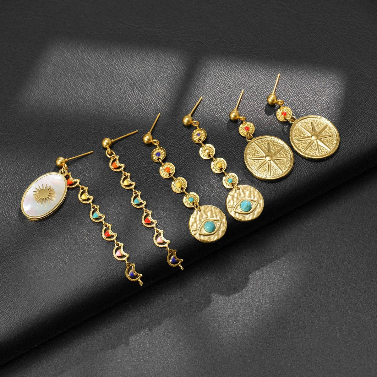 Three pairs of geometric stainless steel drop earrings showing Eight Awn Star, Eye, and Shell Sun designs