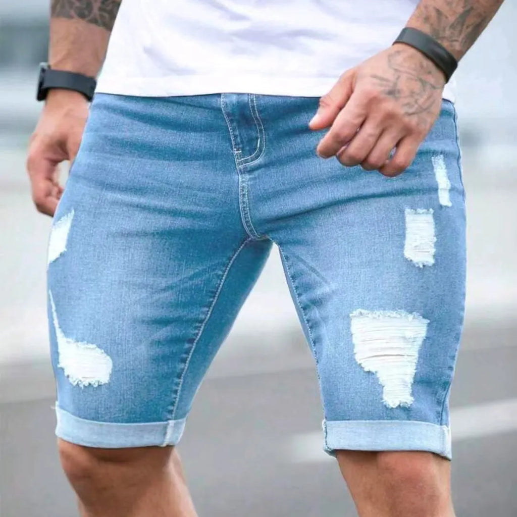 Sky blue men's denim shorts with manual distressing holes on the legs, showing a low waist and zip fly.