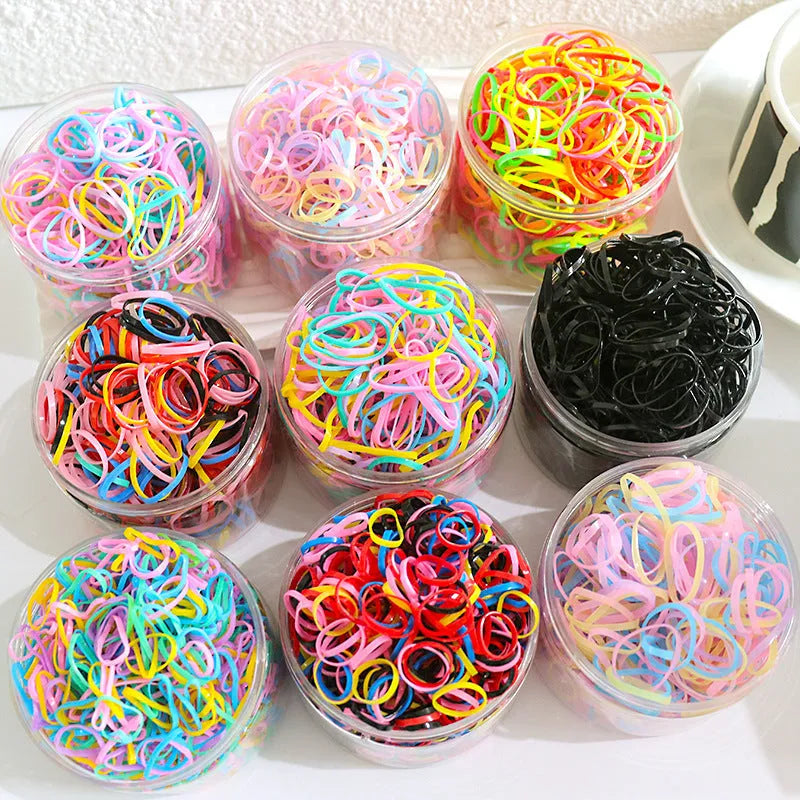 Multi-colour assortment of small TPU elastic baby hair ties in a clear reusable storage container.