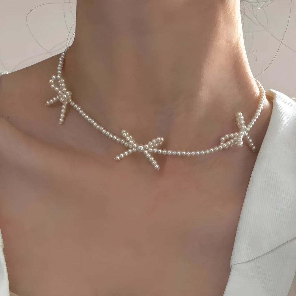 White bow-shaped imitation pearl necklace with an adjustable chain on a woman's clavicle.