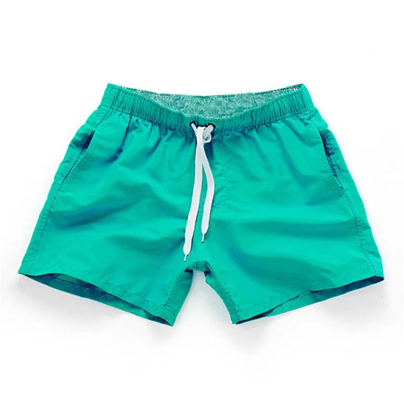 Men's straight-leg beach shorts in emerald green colour on a beach background.