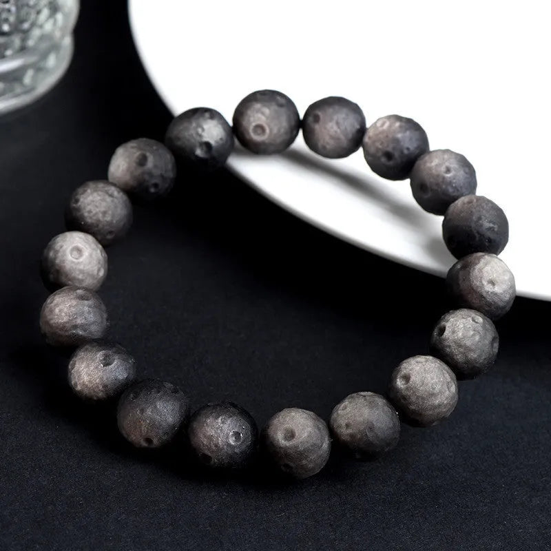 Close-up of a natural obsidian crater ball bracelet with grinding-treated beads on a wrist.